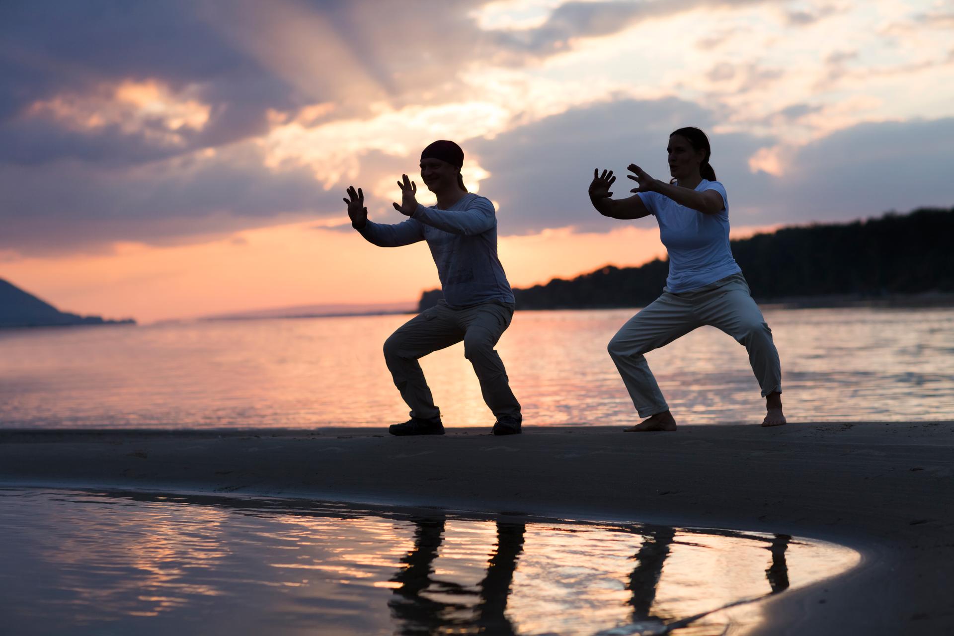 Man and woman doing Tai Chi chuan at sunset on the beach.  solo outdoor activities. Social Distancing. Healthy lifestyle  concept.