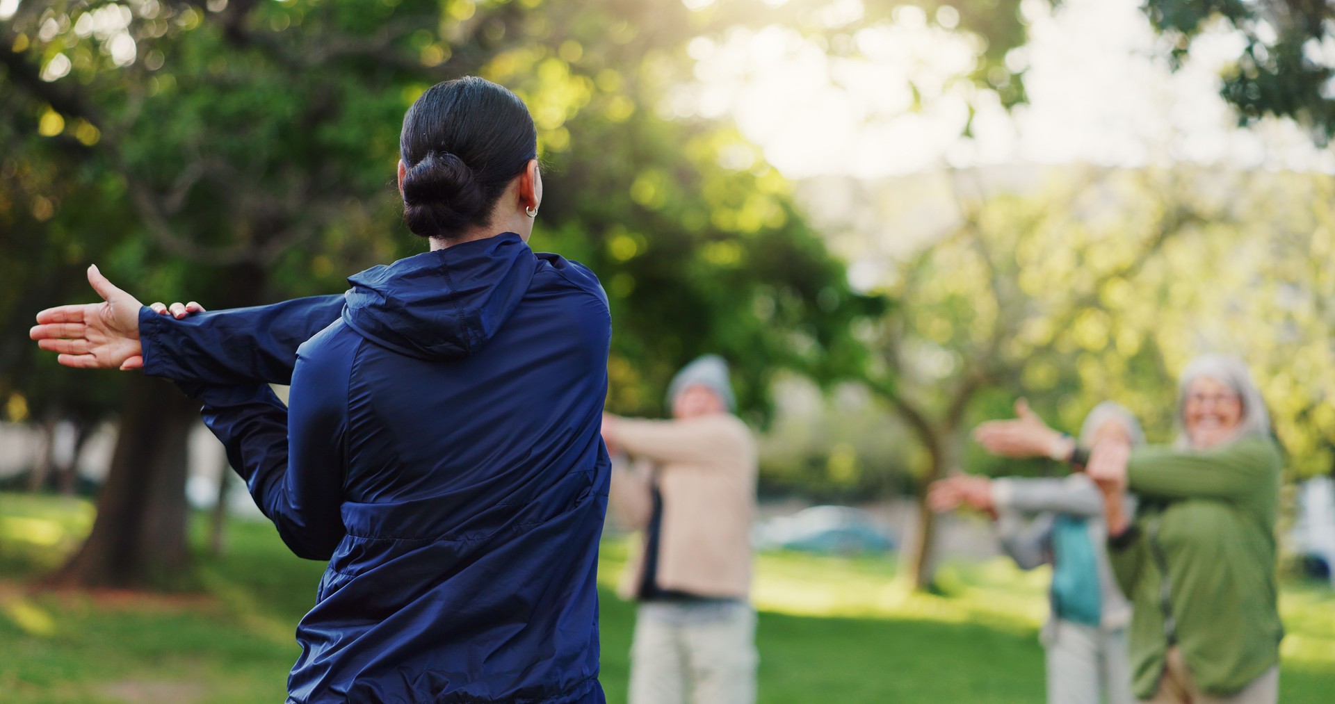 Woman, personal trainer and stretching in nature for elderly care, workout or outdoor exercise. Rear view of female person, coach or instructor training mature group of people at park for fitness