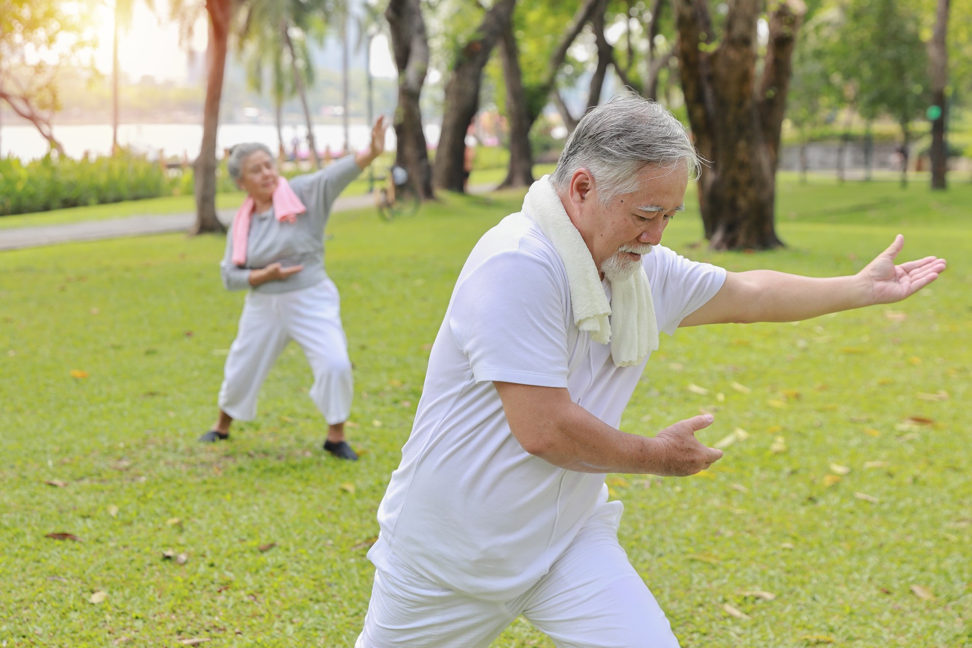 Asian senior couple practice yoga excercise, tai chi tranining, stretching and meditation together with relaxation for healthy in park outdoor after retirement. Happy elderly outdoor lifestyle concept